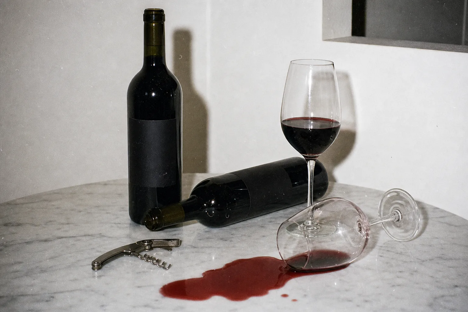 Wine bottles, glasses, corkscrew, and a red wine spill on marble